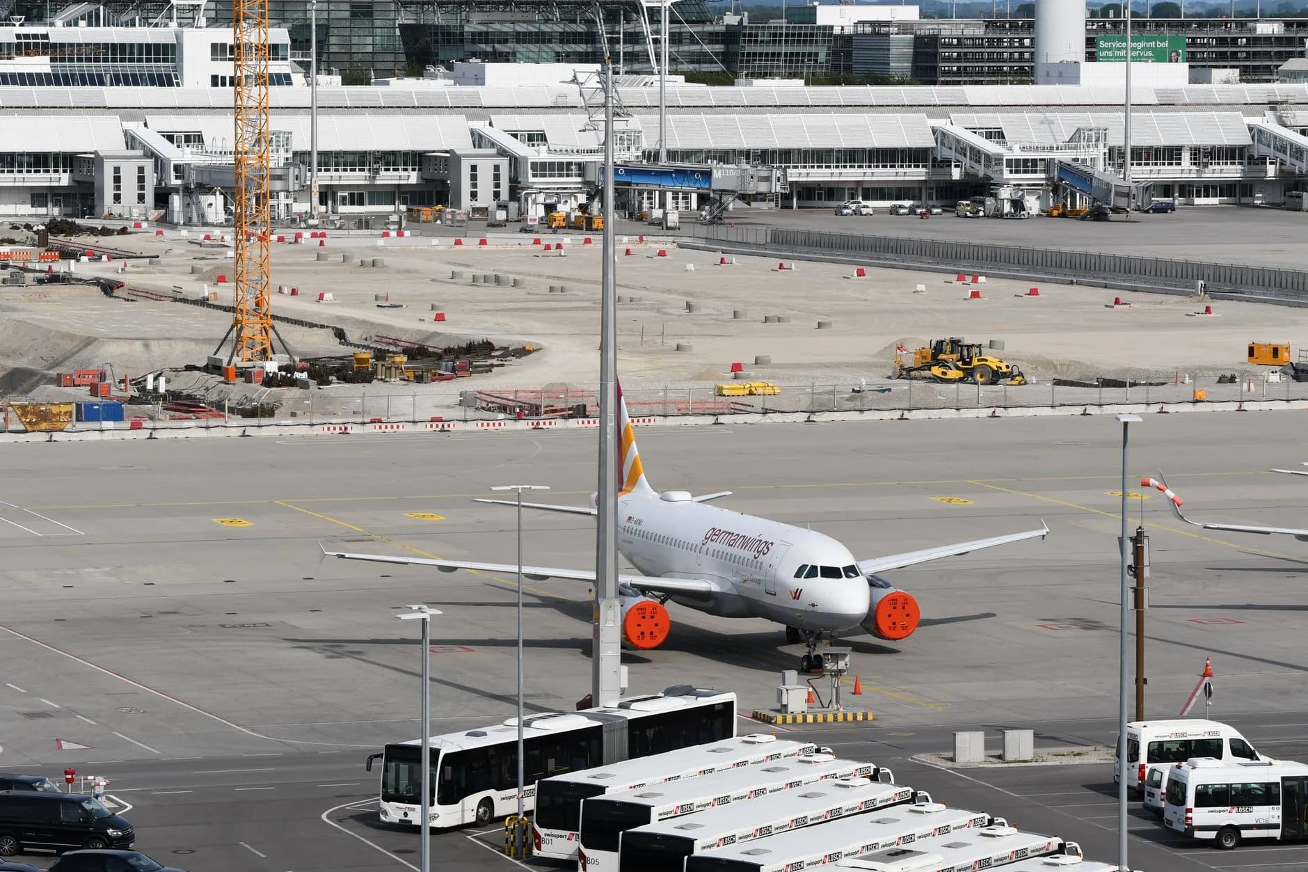 Flugzeug mit Schubabdeckungen steht auf dem Vorfeld vor dem Terminal, davor Flughafenbusse und Baustelle