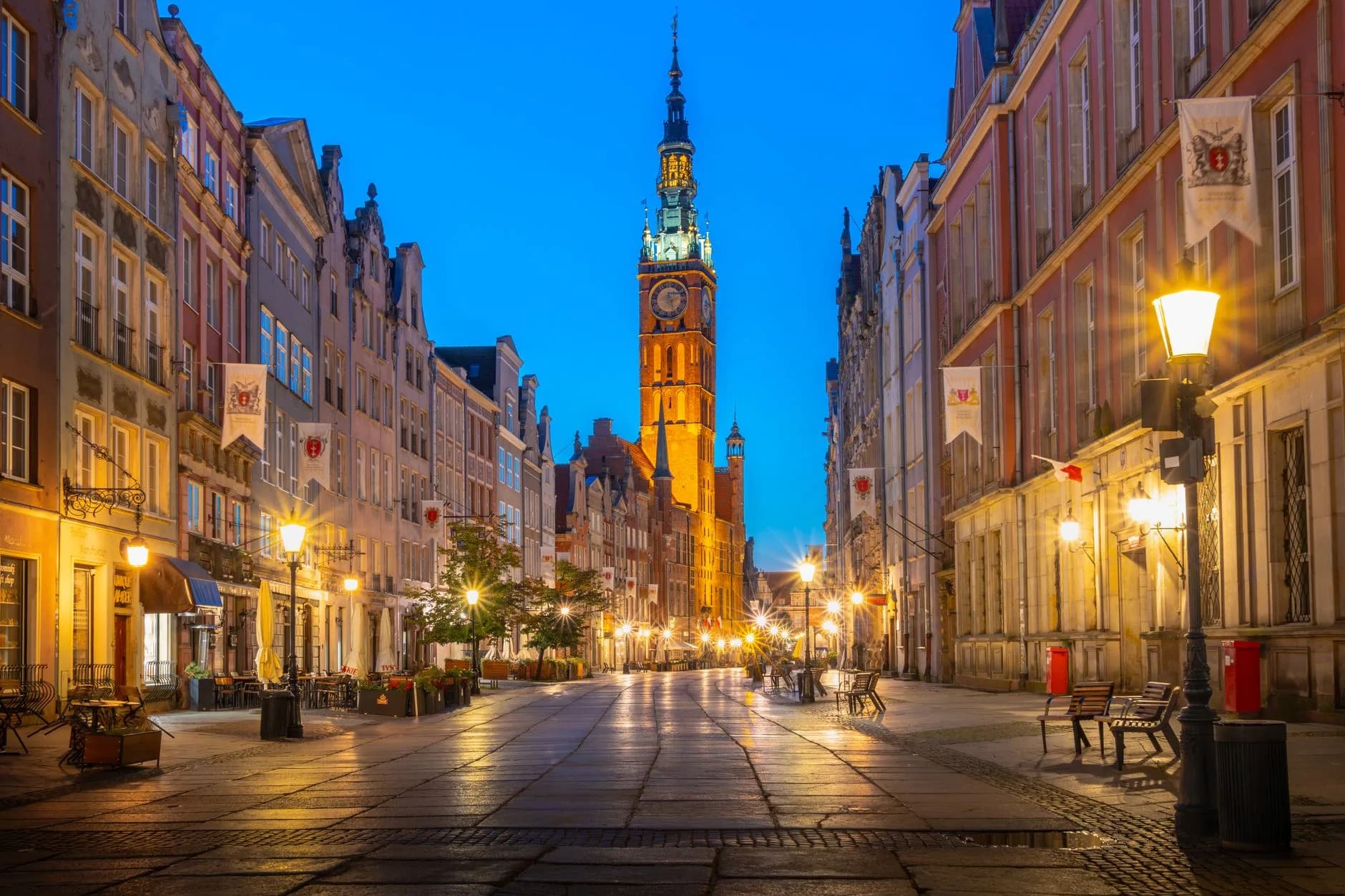 Beleuchtete Altstadtgasse mit historischem Rathausturm in der Abenddämmerung, gesäumte Fassaden und Straßenlaternen