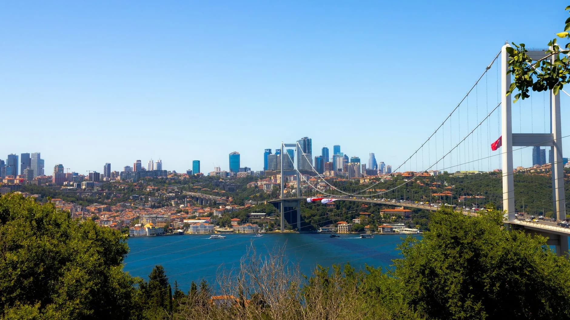 Blick über den Bosporus auf die Hängebrücke und die Skyline Istanbuls mit Hochhäusern und bewaldeten Ufern