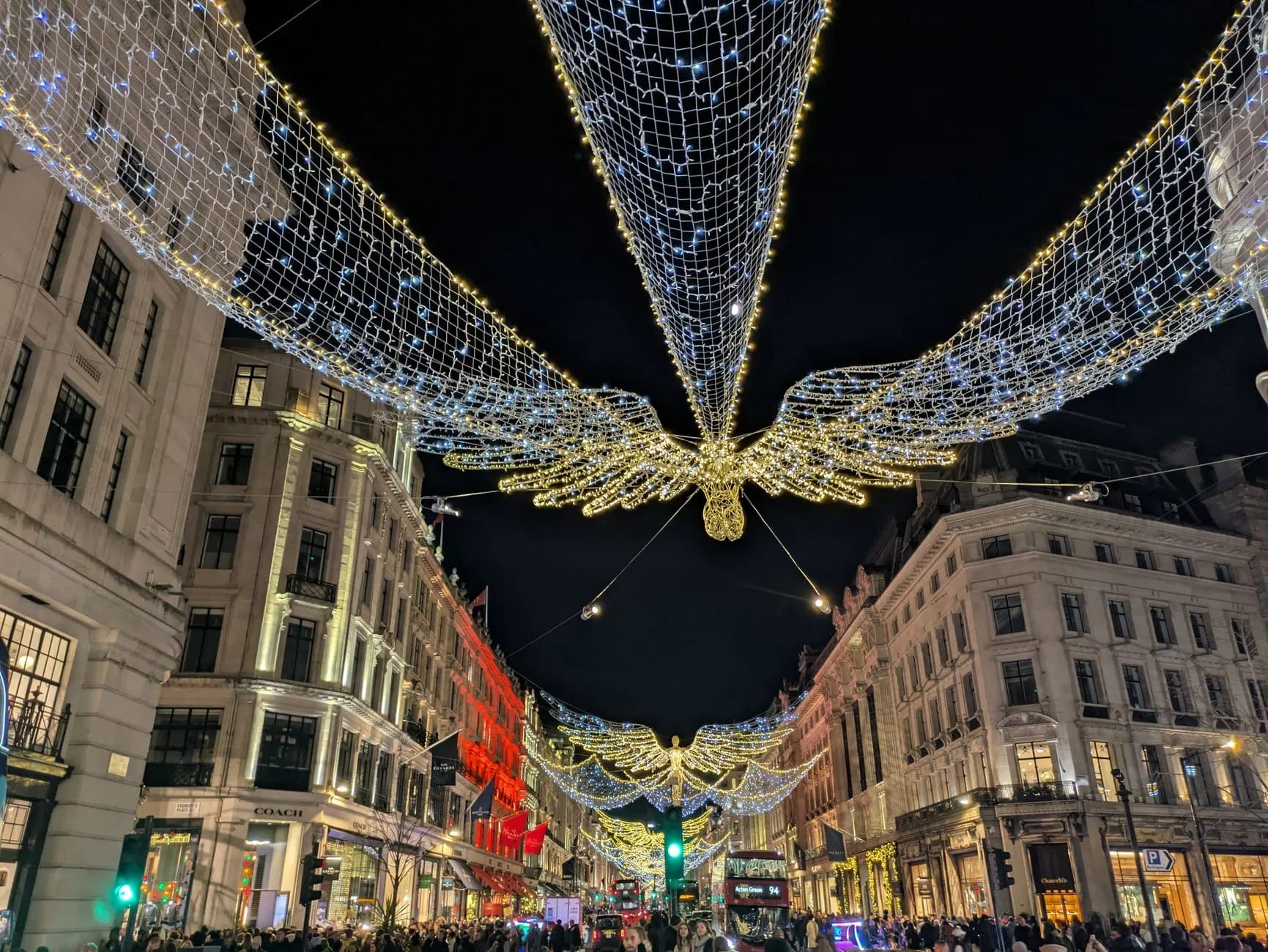 Weihnachtsbeleuchtung mit engelsflügelförmigen Lichterketten über einer belebten Einkaufsstraße bei Nacht