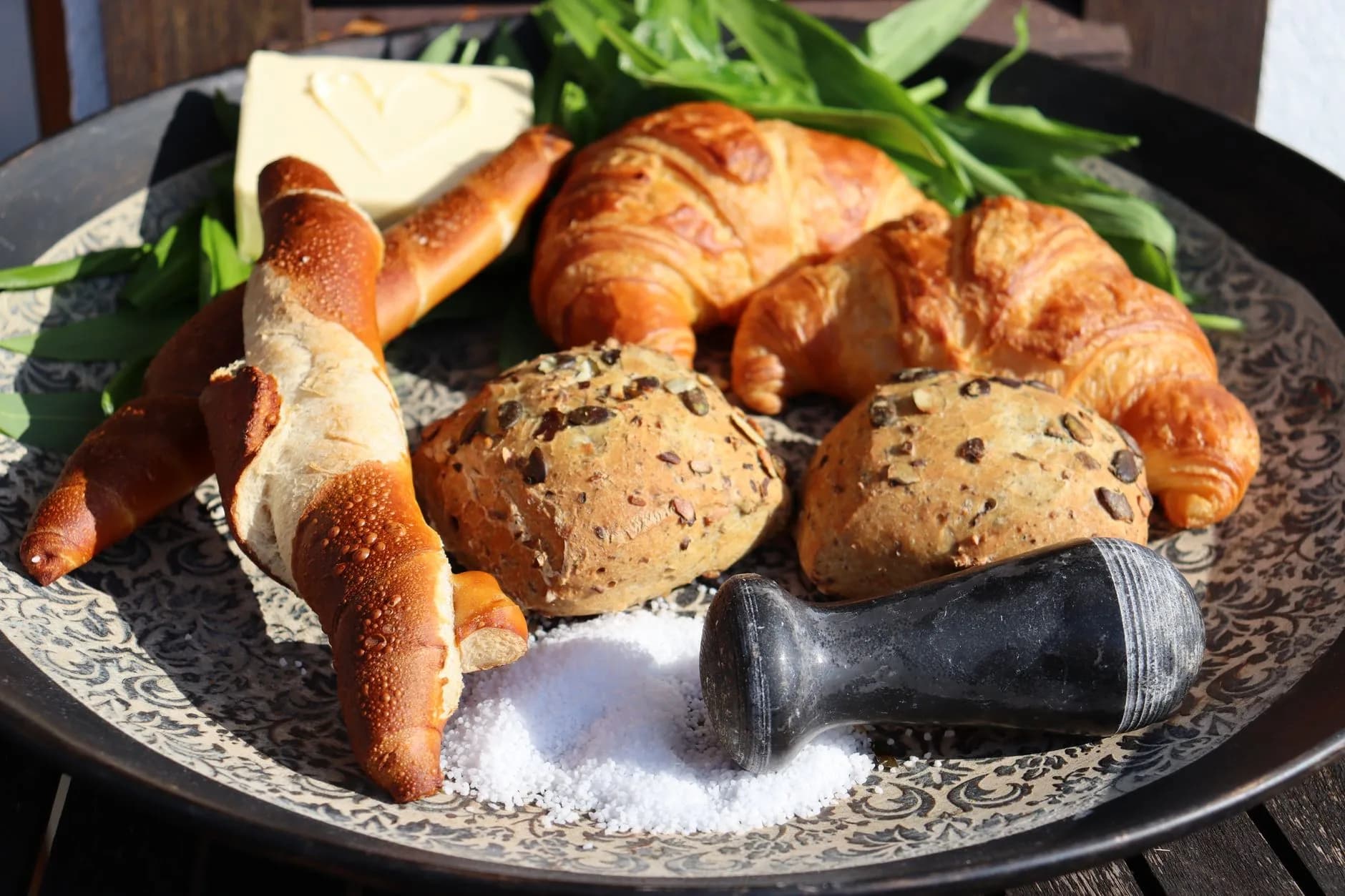 Teller mit Croissants, Laugenstangen und Körnerbrötchen, dekoriert mit Butter, Bärlauch und grobem Salz