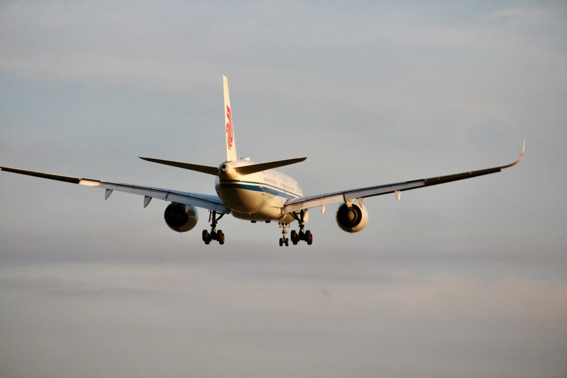 Flugzeug mit ausgefahrenem Fahrwerk im Landeanflug vor bewölktem Himmel, Frontalansicht
