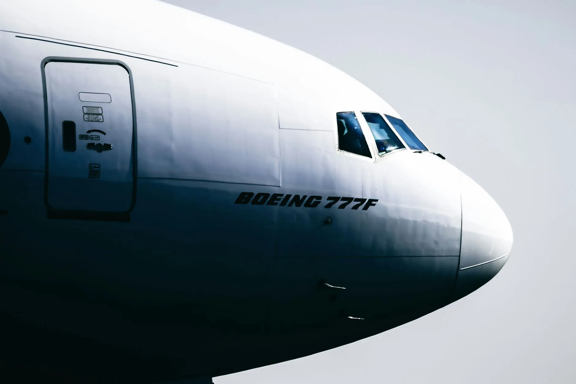 Nahaufnahme des Rumpfbugs einer Boeing 777F mit Cockpitfenster vor grauem Himmel