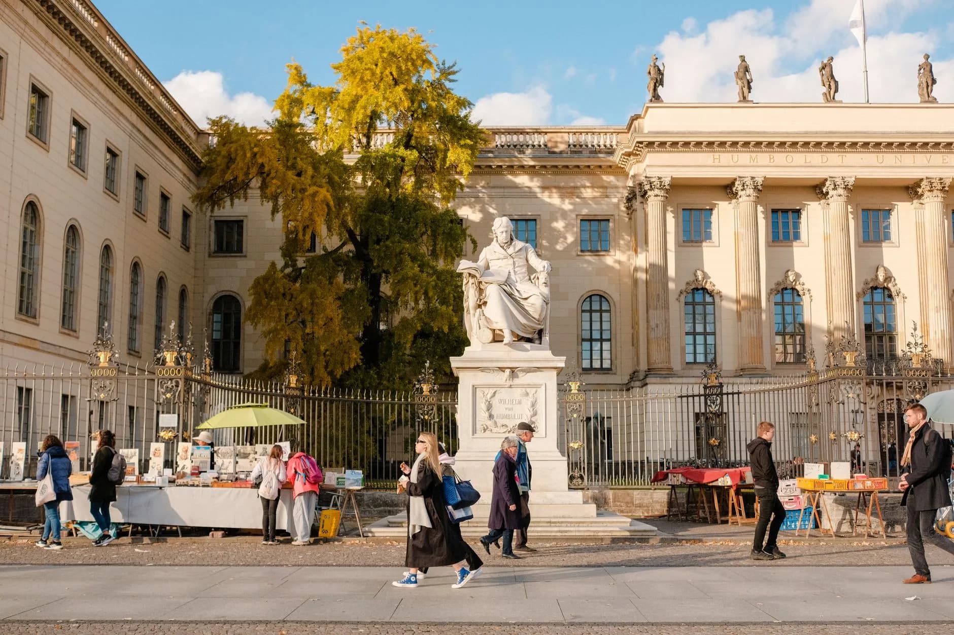 Humboldt-Statue vor der Humboldt-Universität Berlin mit Passanten und Büchermarkt an einem Herbsttag
