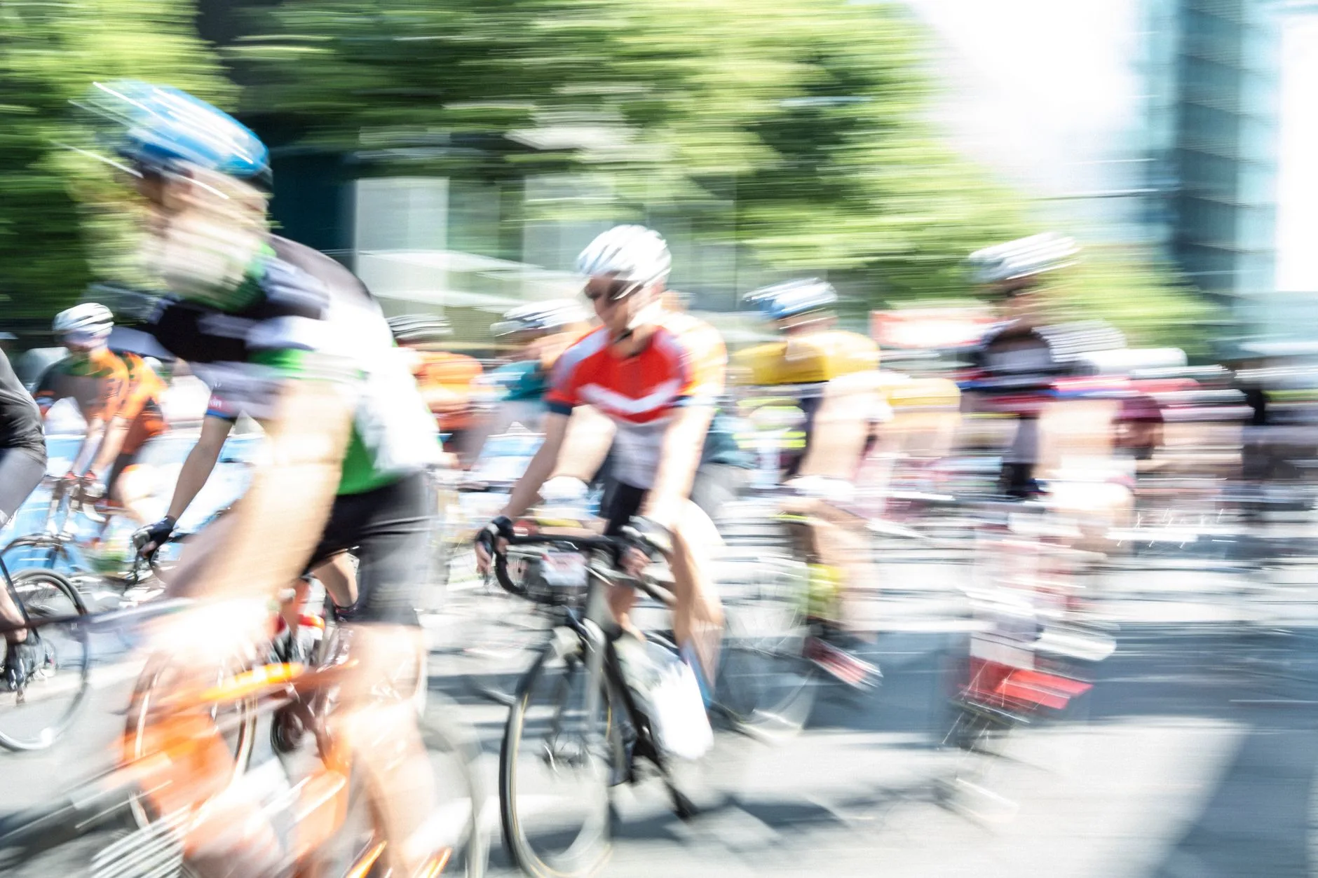 Rennradfahrer mit Helmen fahren in einer Gruppe durch eine Stadtstraße, Bewegungsunschärfe im Bild