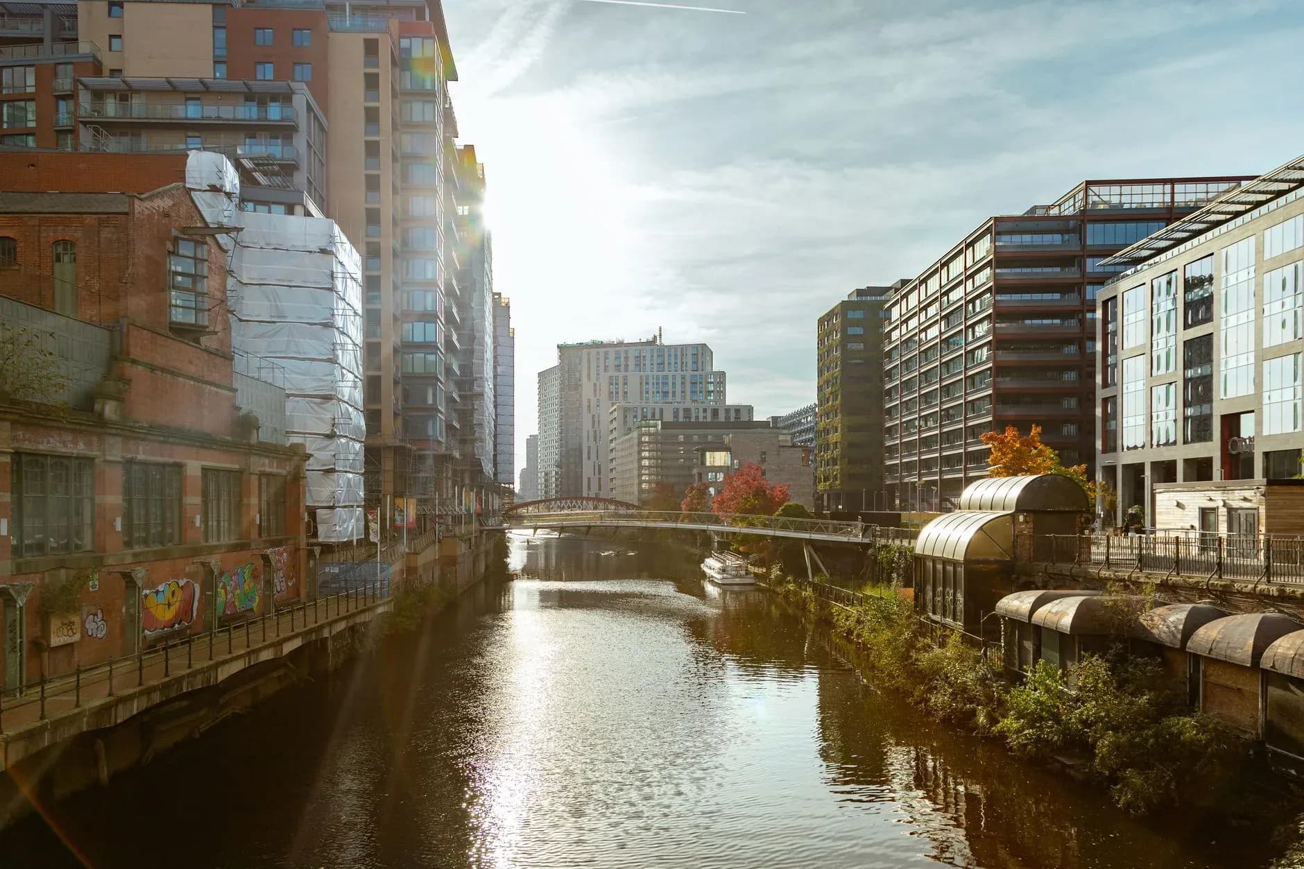 Flusskanal zwischen Hochhäusern und Industriegebäuden einer Stadt, im Hintergrund eine Fußgängerbrücke
