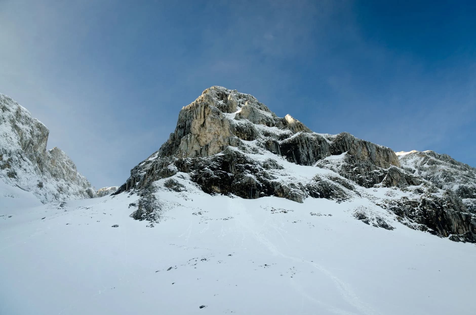 Schneebedeckter Felsgipfel vor klarem blauem Himmel, im Vordergrund ein verschneiter Hang