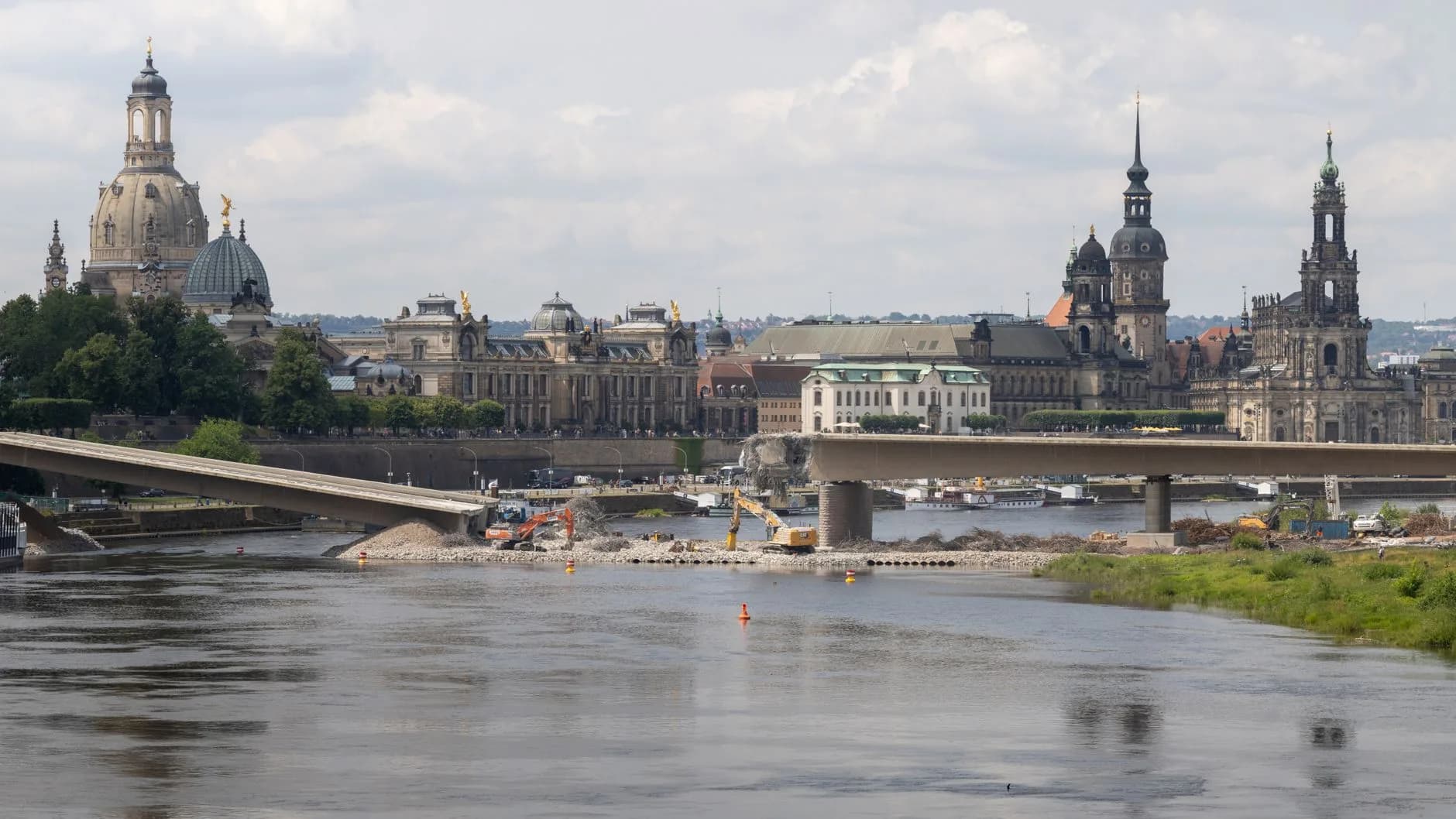 Dresdner Altstadt-Silhouette mit Frauenkirche über der Elbe, im Vordergrund eine eingestürzte Brücke mit Baggern