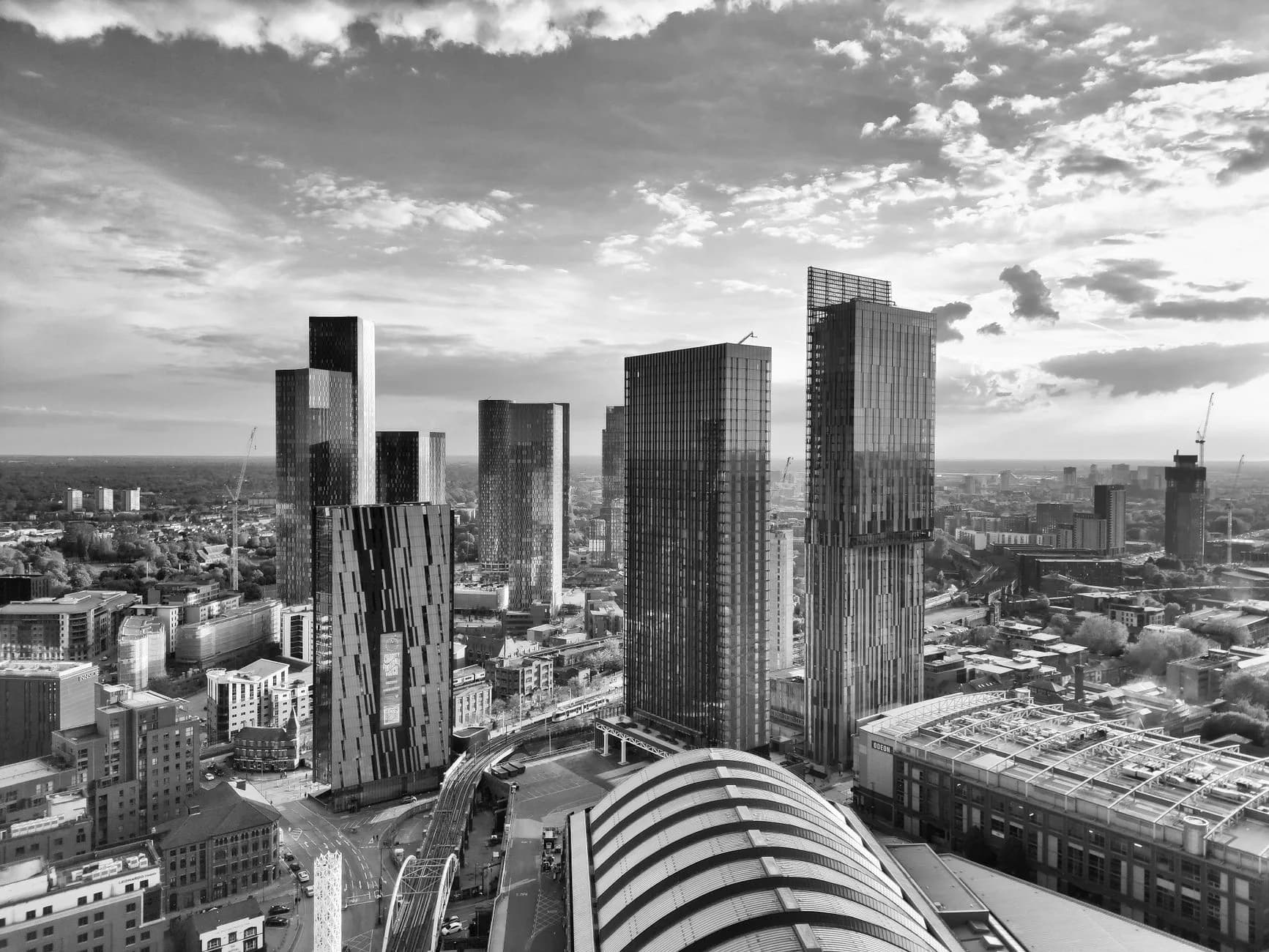 Schwarz-weiße Luftaufnahme einer Großstadt mit mehreren Hochhäusern, Bahnhofsdach und Wolkenhimmel
