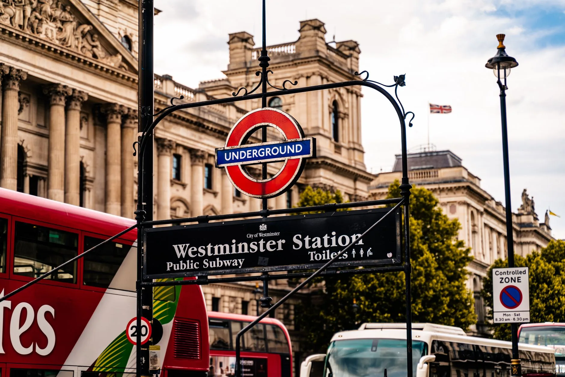 Eingangsschild der Westminster Station mit Underground-Symbol, roten Doppeldeckerbussen und historischen Gebäuden in London
