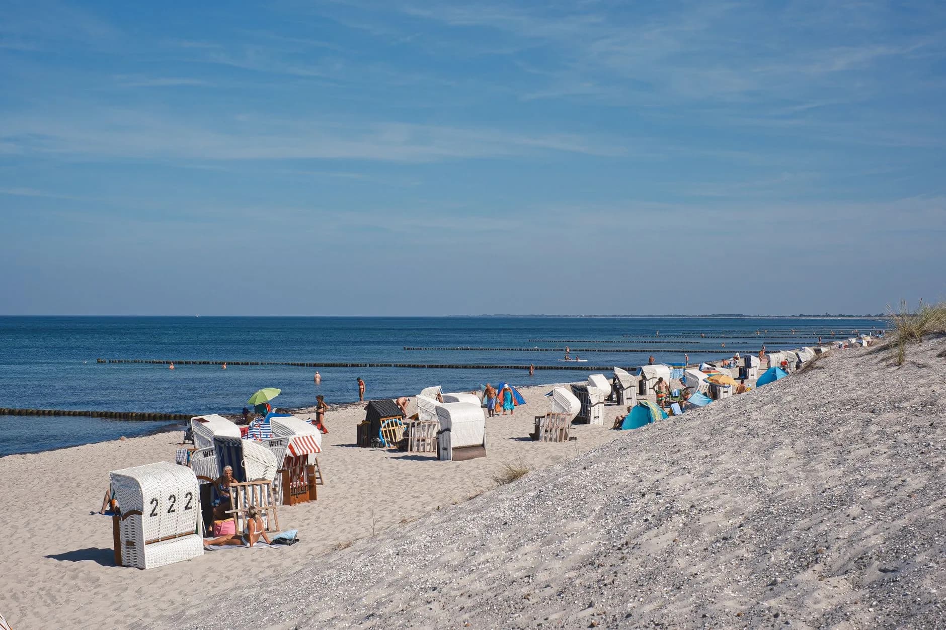 Strand an der Ostsee mit weißen Strandkörben, Badegästen und Buhnen im flachen Wasser