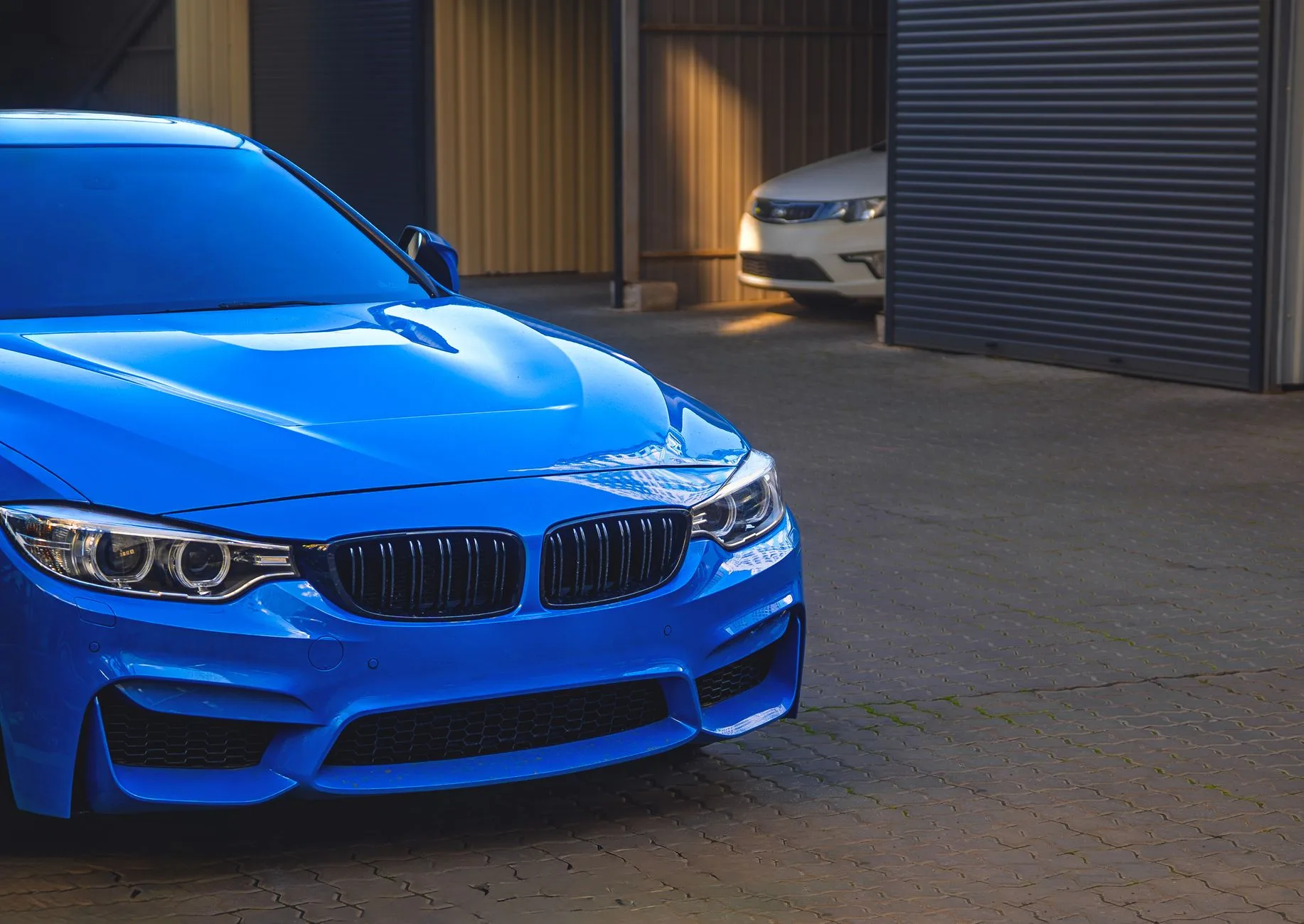 Blauer BMW mit Doppelniere im Vordergrund, dahinter weißer Wagen vor Parkhallen mit Rolltoren