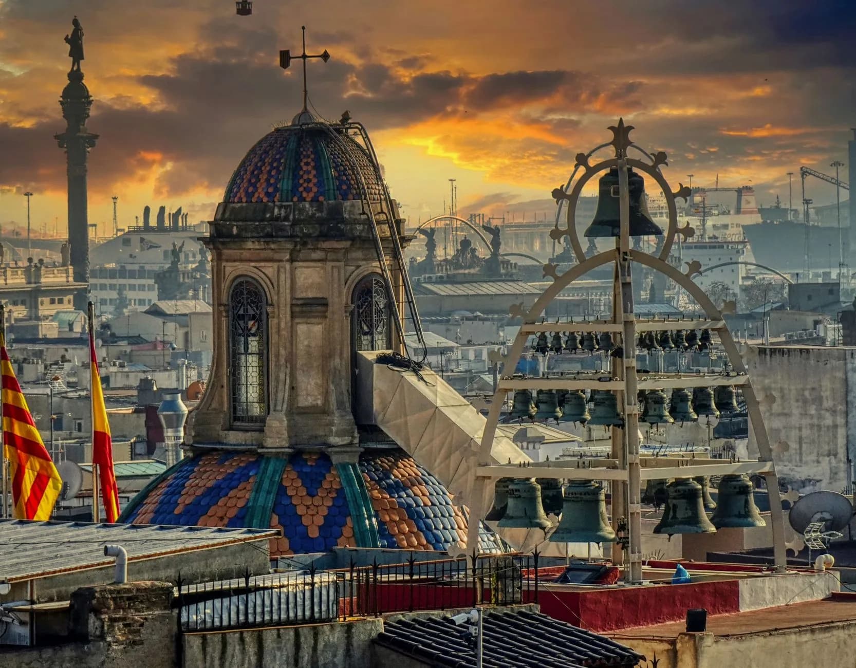 Mosaikverzierte Kirchturmkuppel mit Glockengestell vor Hafenanlage und Fähren bei Sonnenuntergang in Barcelona