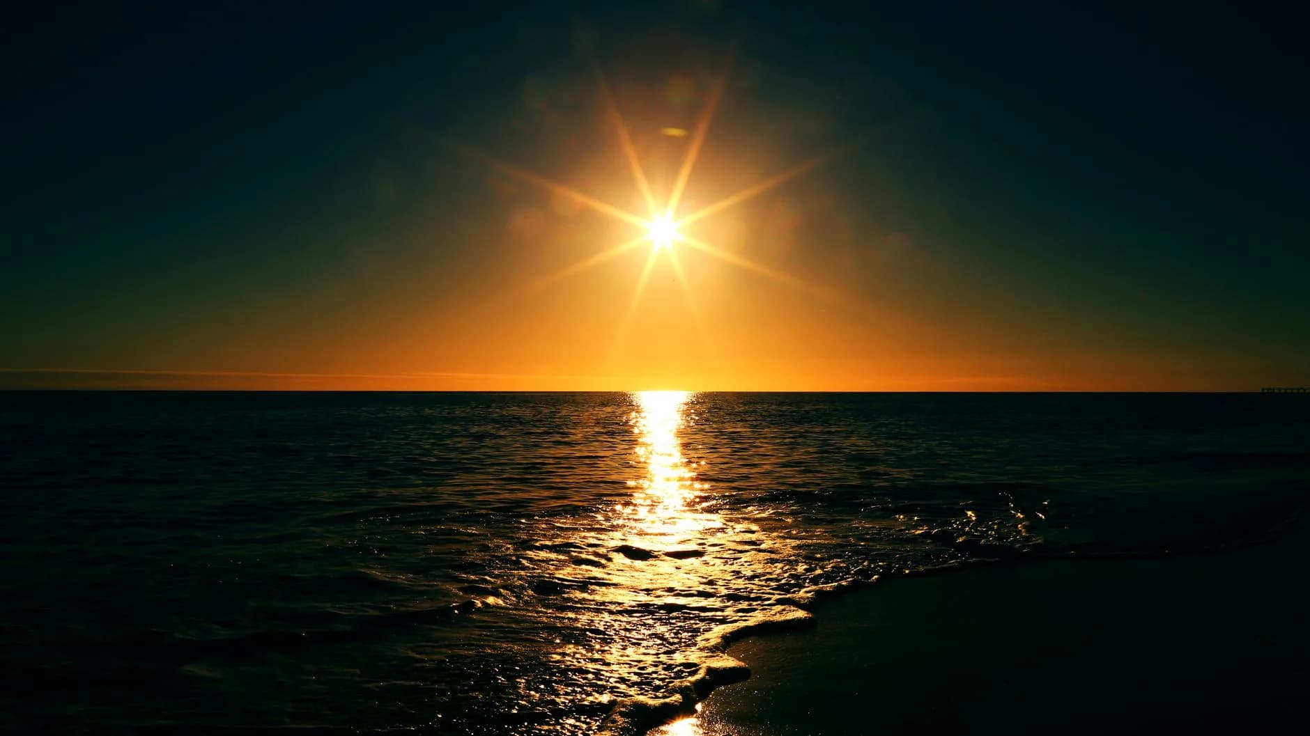 Tief stehende Sonne spiegelt sich als Lichtband auf dem Meer bei Sonnenuntergang