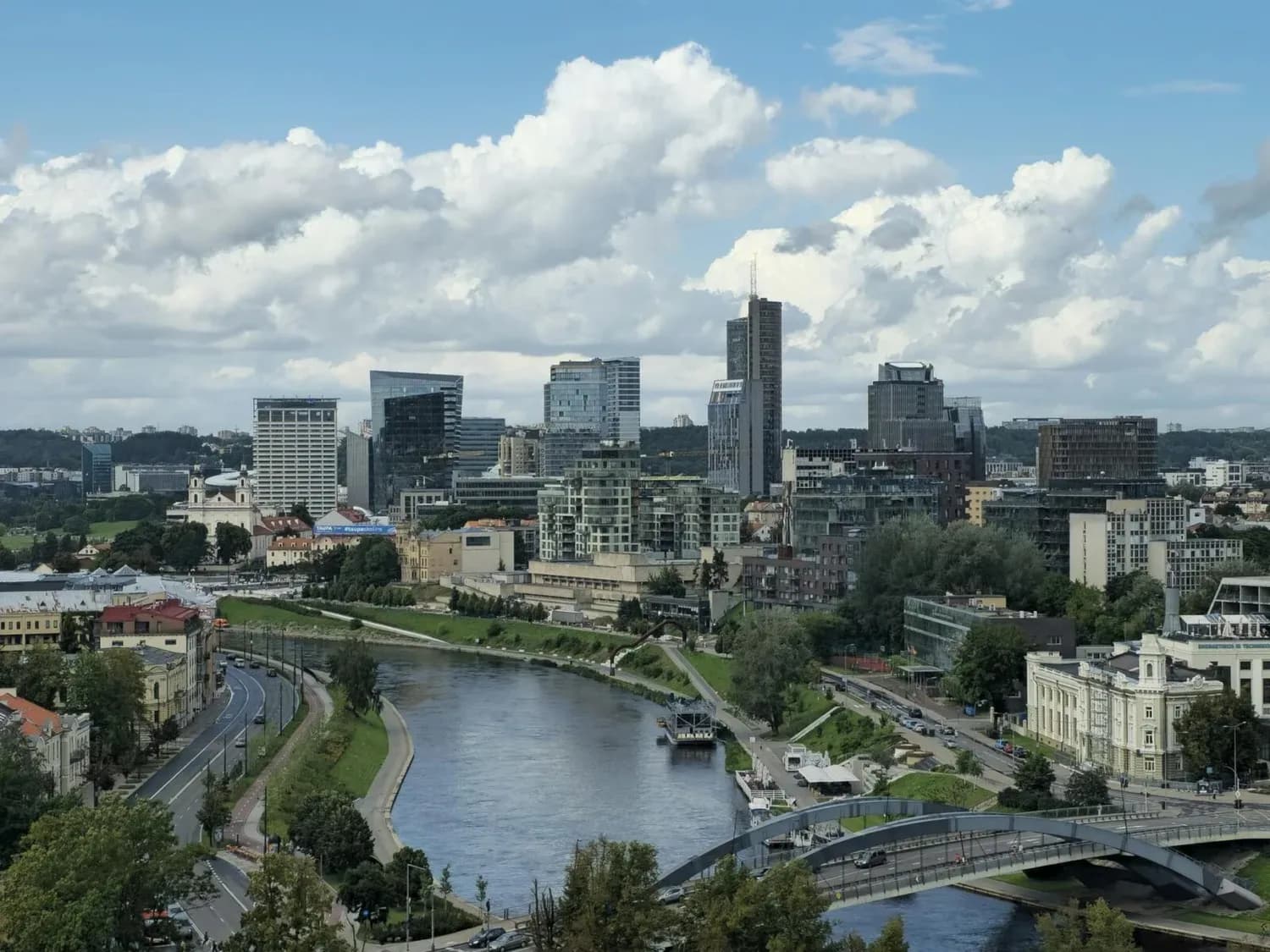 Skyline einer Stadt mit Hochhäusern am Flussufer, Brücke und bewölktem Himmel