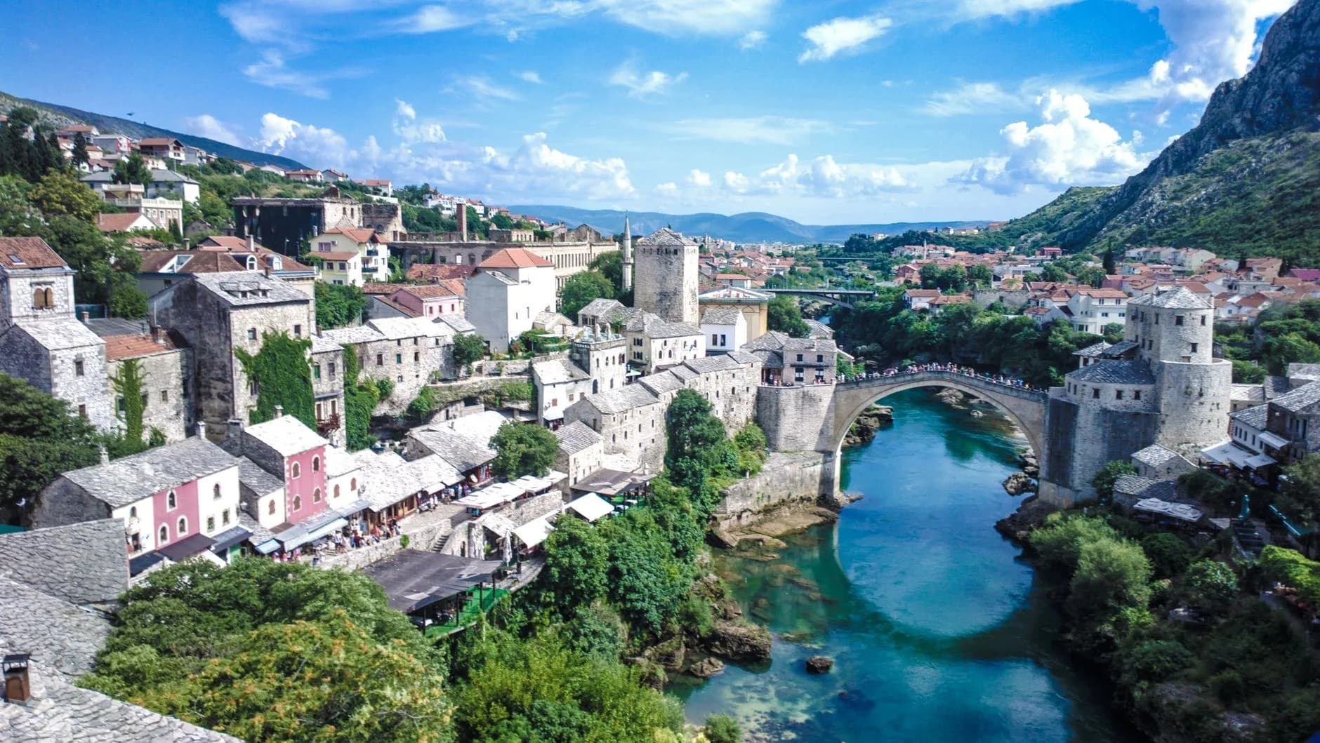 Blick auf die Altstadt von Mostar mit der historischen Steinbrücke über die türkisfarbene Neretva, umgeben von Bergen