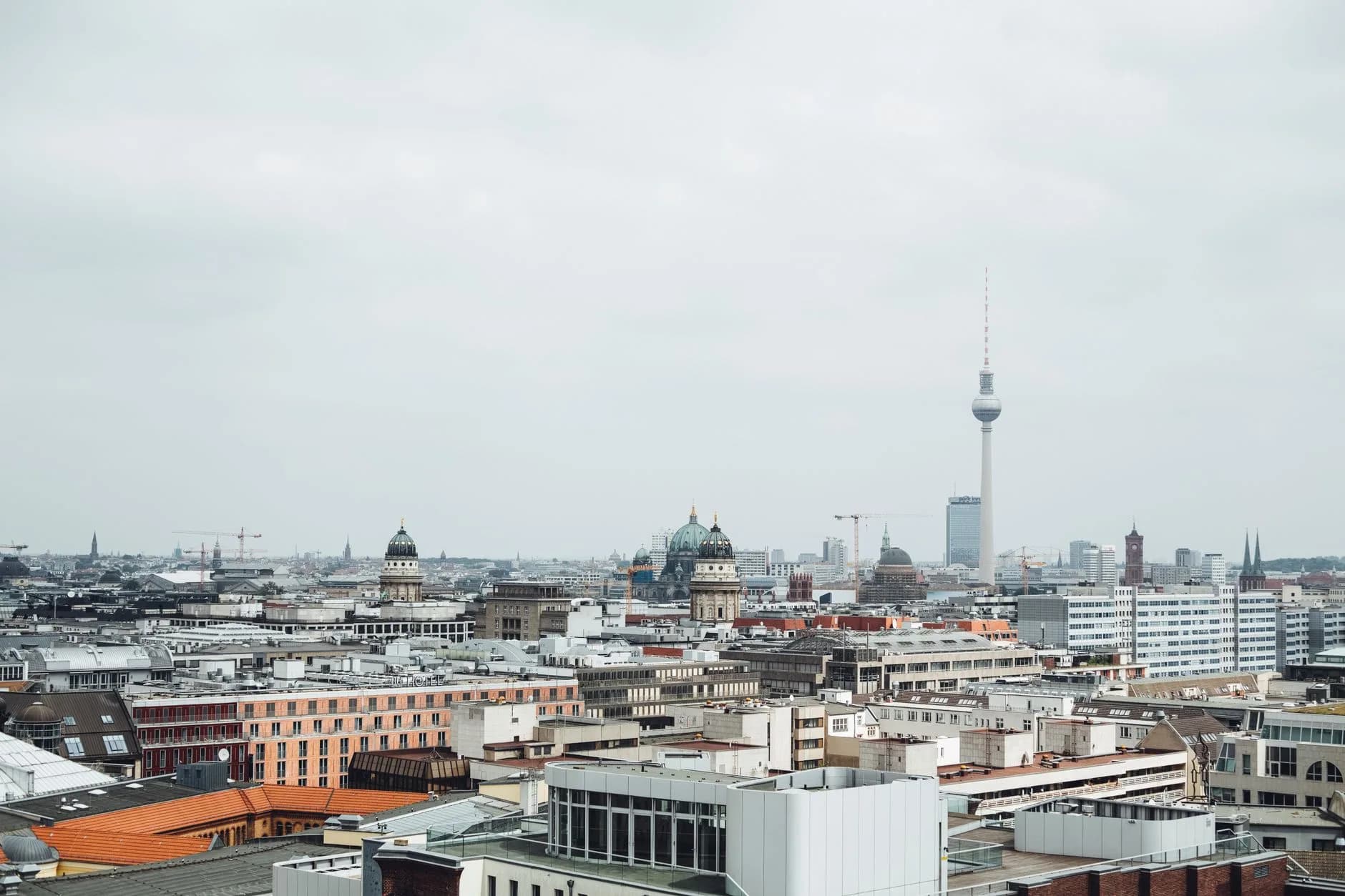 Blick über die Dächer Berlins mit Fernsehturm, Berliner Dom und Baukränen unter bewölktem Himmel