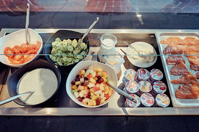 Buffet mit Tomatenscheiben, Gurkensalat, Joghurt, Obstsalat, Joghurtbechern und geräuchertem Lachs.