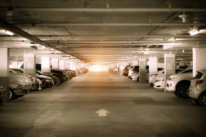Tiefgarage mit Reihen geparkter Autos, Betonpfeilern mit Sektorkennzahlen und Lichtschein am fernen Ende.