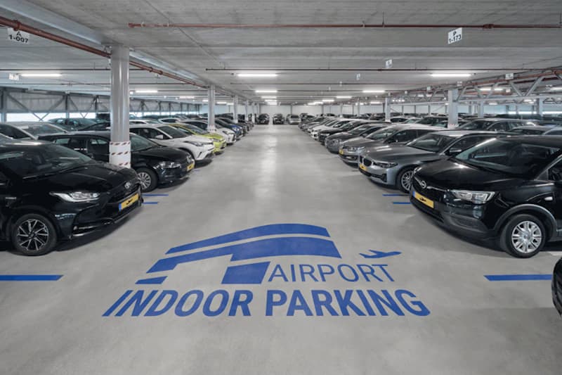 Überdachtes Parkhaus mit breitem Gang, zwei Reihen geparkter Autos und Bodenmarkierung in der Bildmitte.
