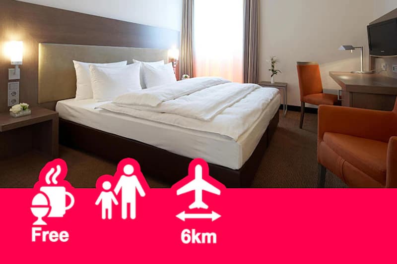 Doppelzimmer mit großem Bett, Nachttischen, Wandlampen, Schreibtisch und zwei orangefarbenen Stühlen.