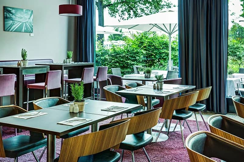 Speiseraum mit gedeckten Tischen, Holzstühlen, Topfpflanzen und großen Fenstern zur Terrasse mit Sonnenschirmen.
