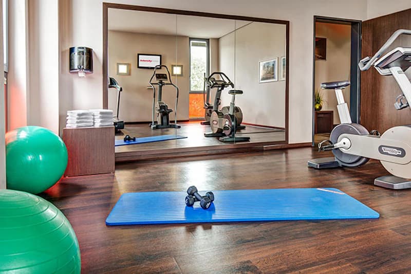 Hoteltrainingsraum mit blauer Gymnastikmatte und zwei Hanteln, grünen Gymnastikbällen, Fahrradergometern und Spiegelwand.