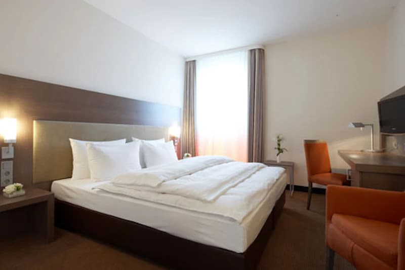 Helles Hotelzimmer mit Doppelbett, Nachttischen, Lampen und Schreibtisch.