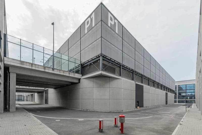 Mehrstöckiges graues Parkhaus mit großer P1-Beschriftung, gläserner Fußgängerbrücke und roten Pollern im Vordergrund.