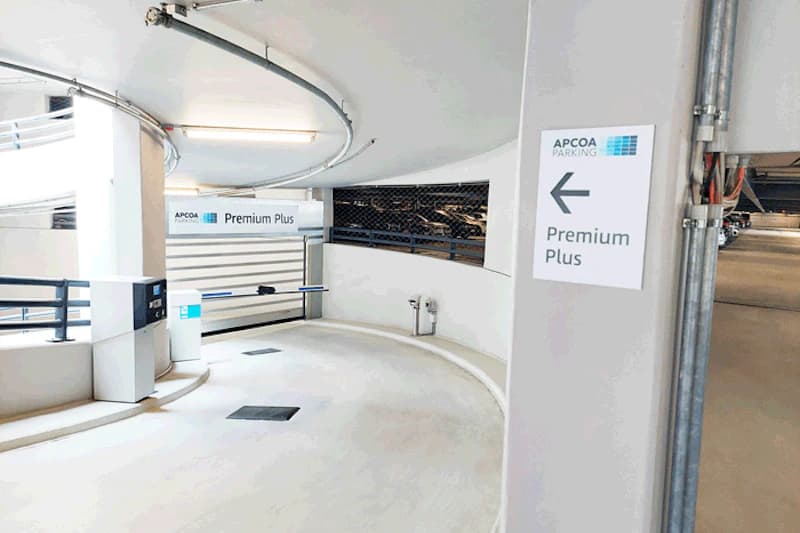 Innenrampe eines Parkhauses mit Schranke, APCOA-Schild Premium Plus und kurviger Auffahrt.