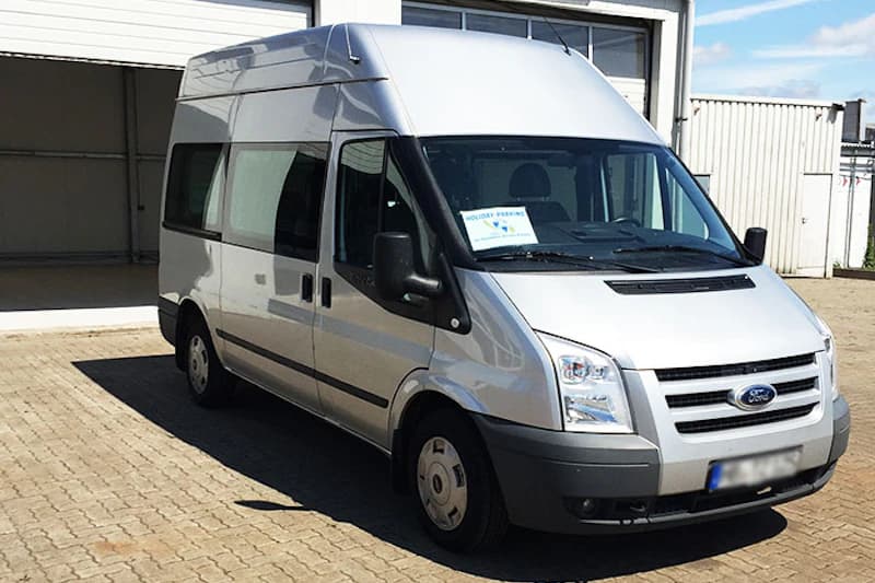 Silberner Shuttle-Van mit Holiday Parking Hinweis auf dem Armaturenbrett vor einer Garagenöffnung.