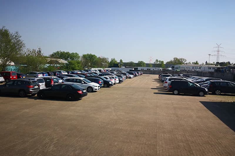 Gepflasterter Parkplatz mit zwei Reihen parkender Autos und freier Fläche in der Mitte.