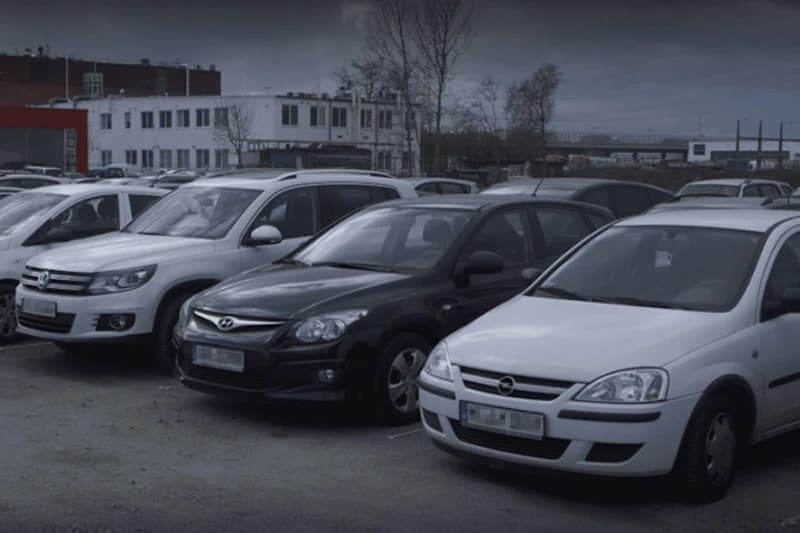 Mehrere geparkte Autos auf einem Außenparkplatz vor einem mehrstöckigen Gebäude.