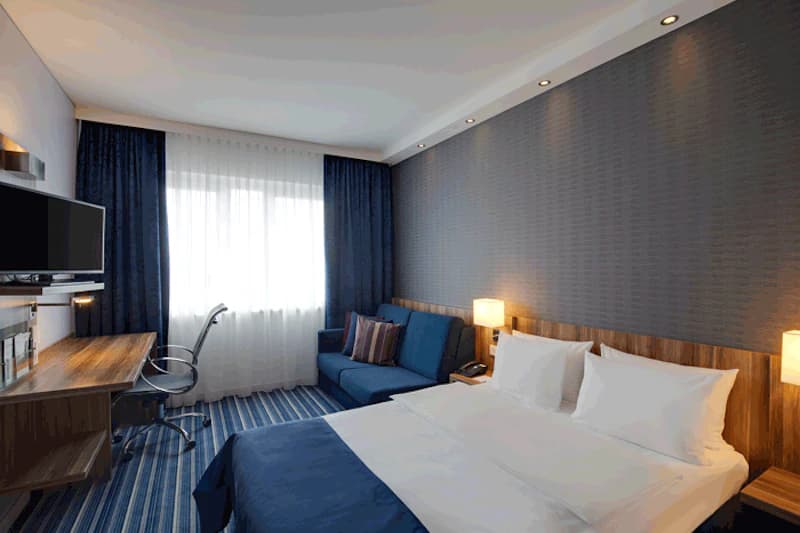 Hotelzimmer mit Doppelbett, Sofa, Schreibtisch, Stuhl und Fernseher.