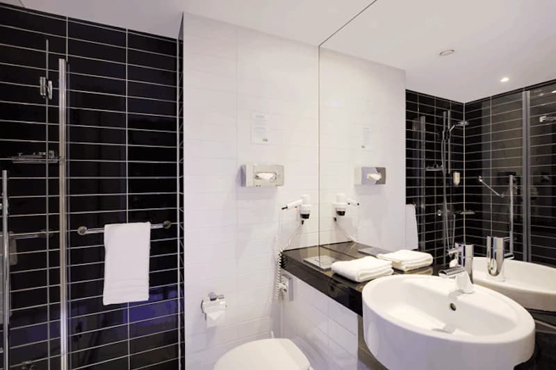 Hotelbadezimmer mit Waschbecken, Spiegel, Duschkabine, Toilette, Handtüchern und Wandfön.