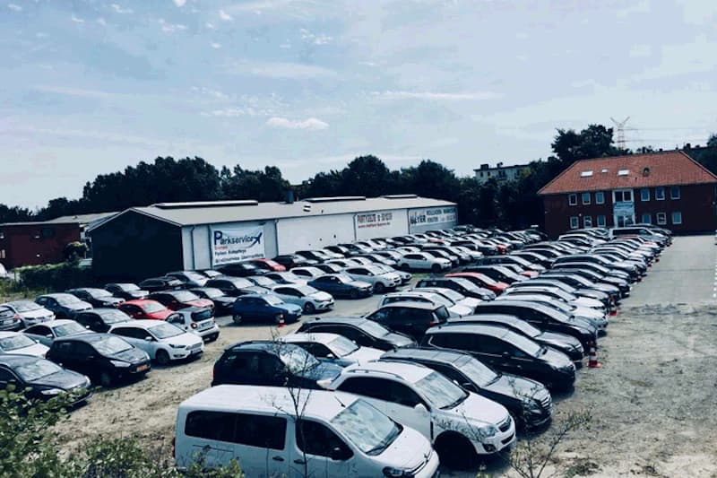 Großer Außenparkplatz mit zahlreichen geparkten Autos und einer Halle mit Parkservice-Schriftzug.
