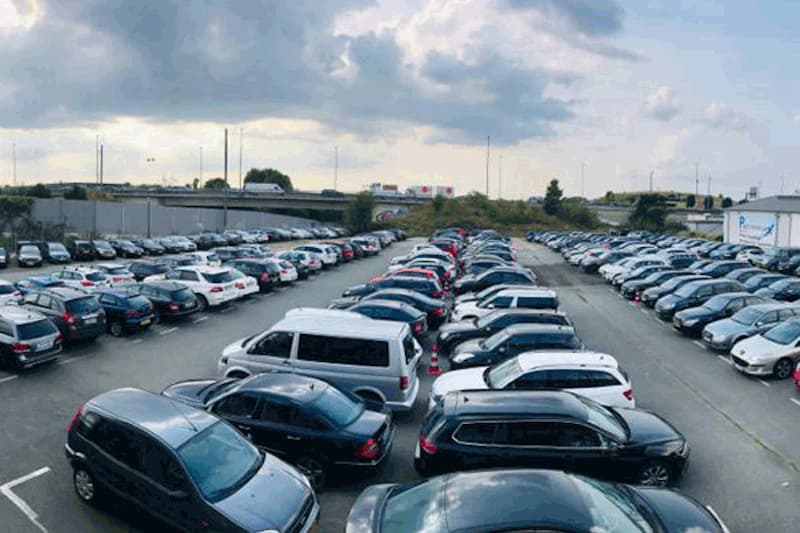 Außenparkplatz mit dichtstehenden Reihen geparkter Autos und trübem Himmel.
