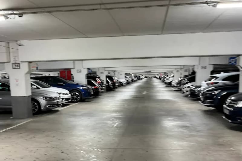Parkhausgang mit Reihen geparkter Autos an beiden Seiten und Mittelzufahrt unter Deckenbeleuchtung.