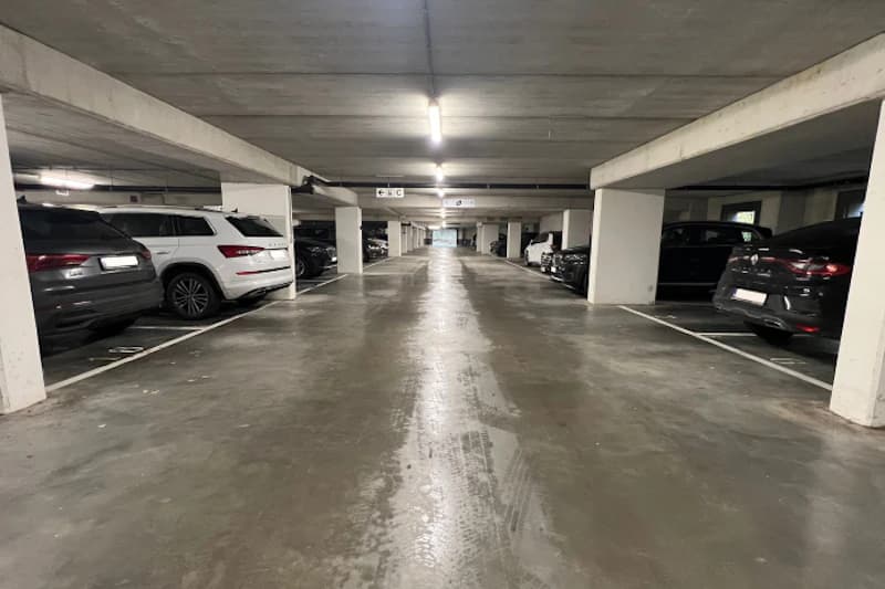 Tiefgaragenparkhaus mit Mittelgang, Betonpfeilern und geparkten Autos beidseitig.