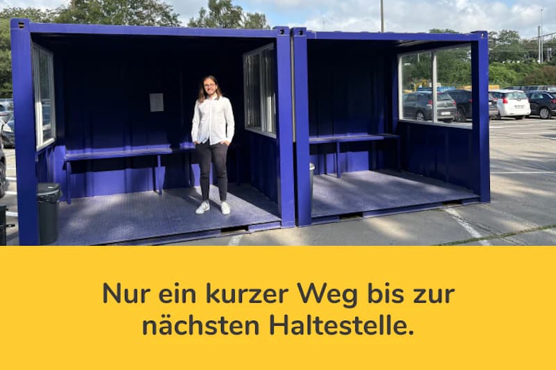 Zwei blaue Containerwartebereiche auf einem Parkplatz, eine Frau steht im linken, geparkte Autos im Hintergrund.
