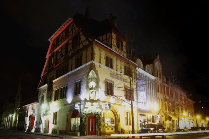 Beleuchtetes historisches Hotelgebäude mit Fachwerkgiebel, roter Eingangstür und Straßenlaternen bei Nacht.