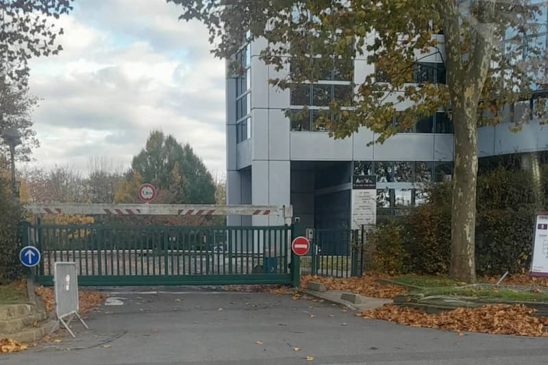 Geschlossene grüne Torzufahrt mit Schranke, Verkehrsschildern, Bürogebäude und Herbstlaub am Boden.