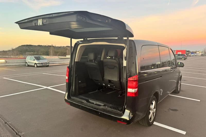 Schwarzer Kleinbus mit geöffneter Heckklappe auf großem, markiertem Parkplatz bei Sonnenuntergang.
