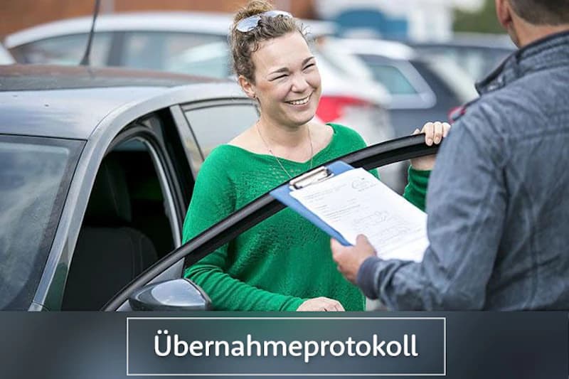 Frau in grünem Pullover an offener Autotür lächelnd, Mann hält ein Klemmbrett mit Formular.