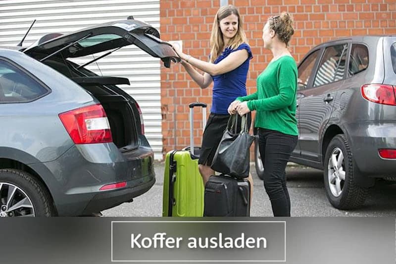 Zwei Frauen entladen Koffer am offenen Kofferraum eines grauen Autos auf einem Parkplatz.