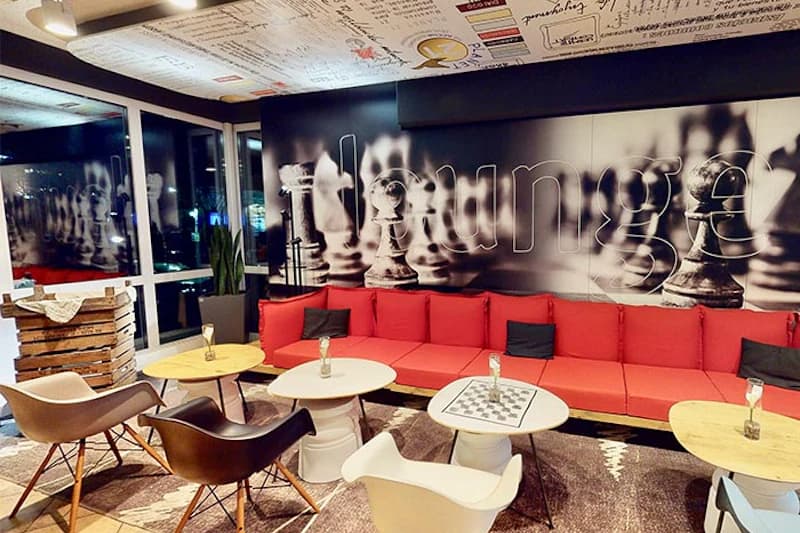 Rote Sofazeile, Tische und Stühle in Hotellounge vor schwarzweisser Wand mit übergrossen Schachfiguren.