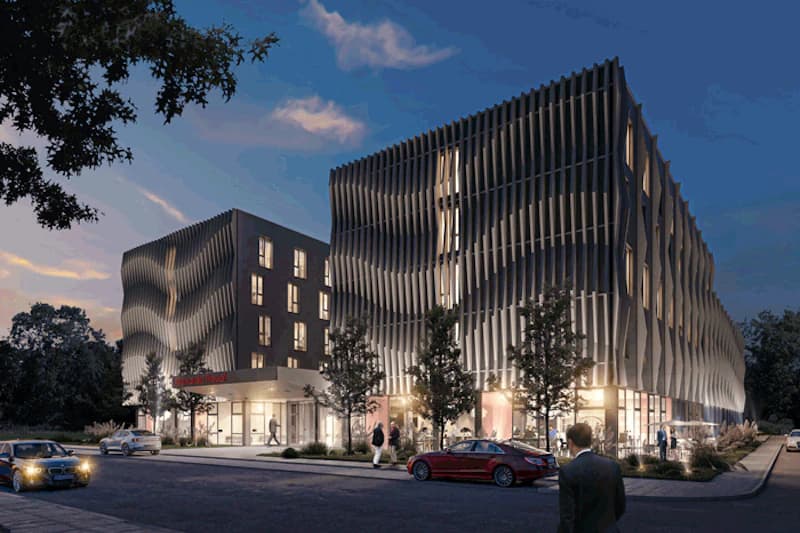 Abendaufnahme eines modernen Hotels mit wellenförmiger Fassade, beleuchteten Fenstern, Autos und Passanten.