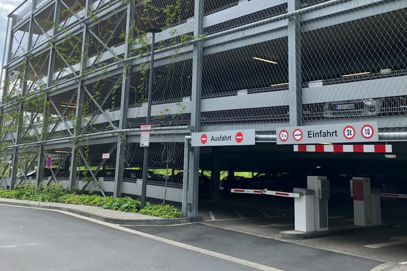 Mehrstöckiges Parkhaus mit Metallgitterfassade, Einfahrt mit Schranke und Ausfahrtszeichen.