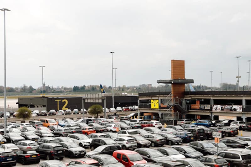 Großer Parkplatz mit dicht geparkten Autos vor Terminal T2 am Flughafen Charleroi und mehrstöckiger Zufahrt.