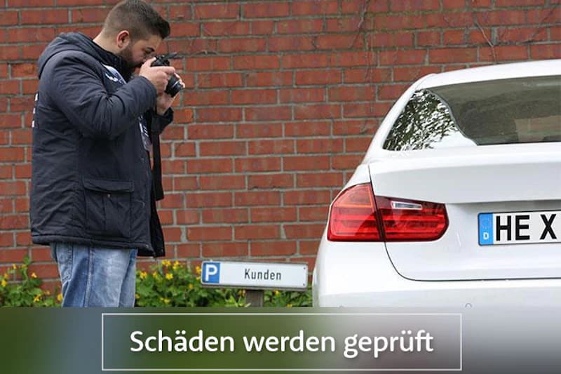 Mann fotografiert Heck eines weißen Autos vor roter Backsteinwand neben Parkplatzschild Kunden.
